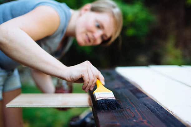 Jeune femme qui applique une couche de lasure sur du bois pour le protéger