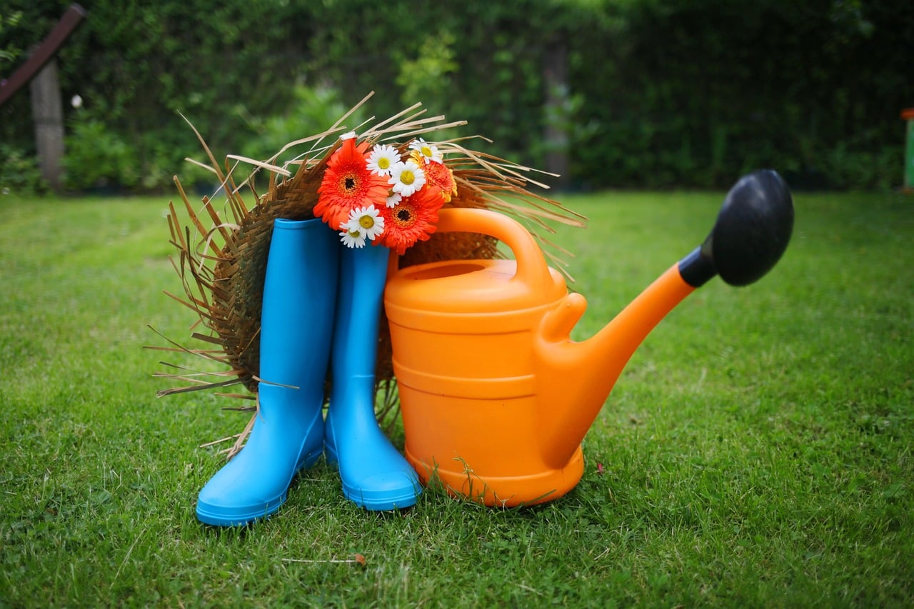 bottes en caoutchouc bleues, arrosoir orange, bouquet de fleurs et chapeau de paille