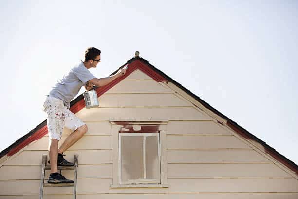 Homme qui repeint sa maison lors de sa rénovation extérieure